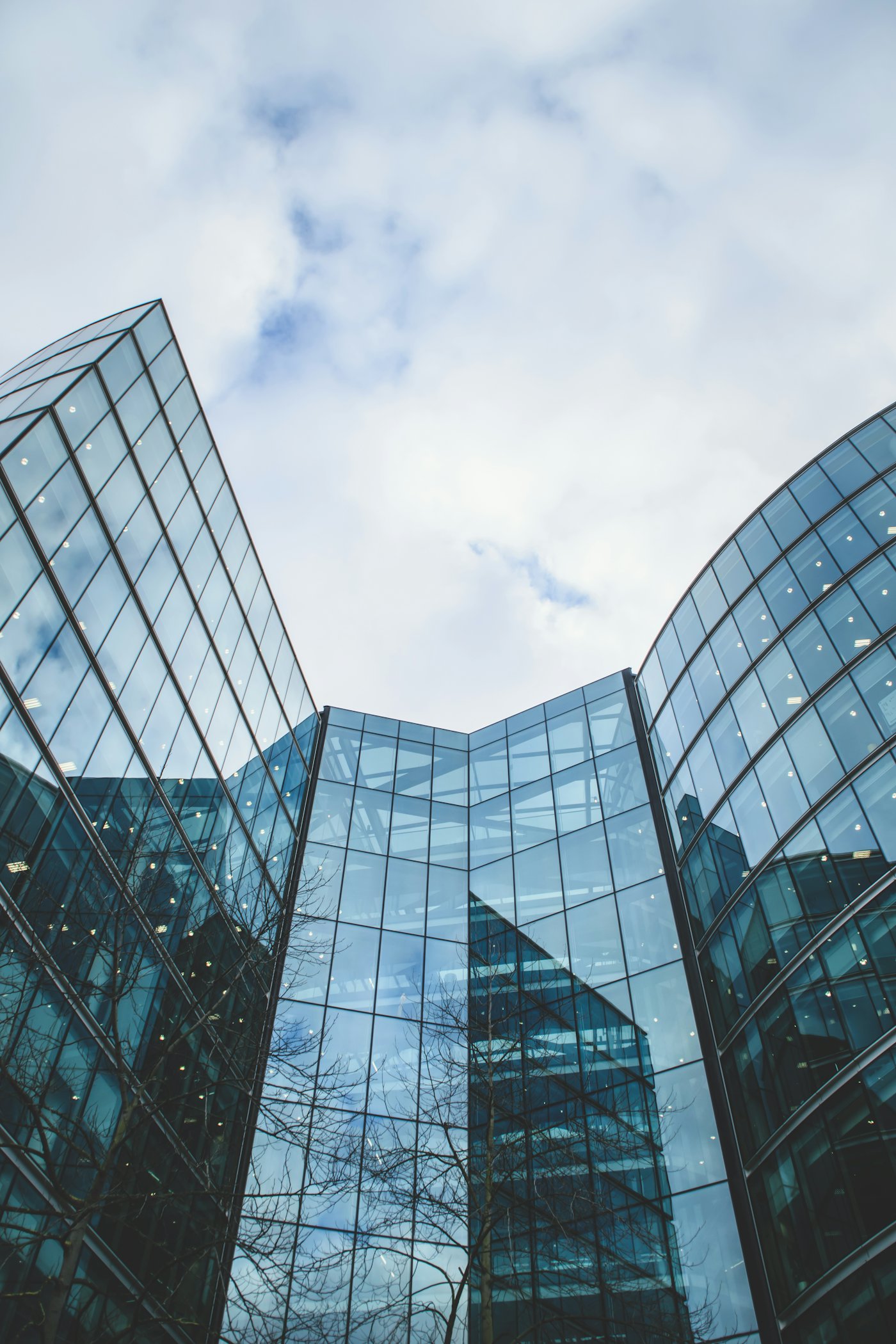 Two glass office buildings rising against a cloudy sky, one with a straight face and one with a curved face.