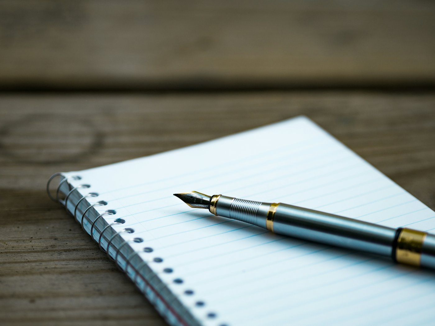 A fountain pen lying across a blank lined page of a spiral notebook.